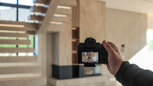 A photographer holding a camera and capturing a modern interior with a staircase and a fireplace