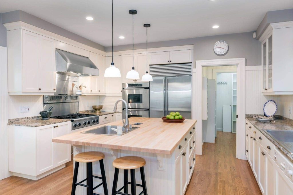 A kitchen interior in white with a wooden floor and a kitchen island